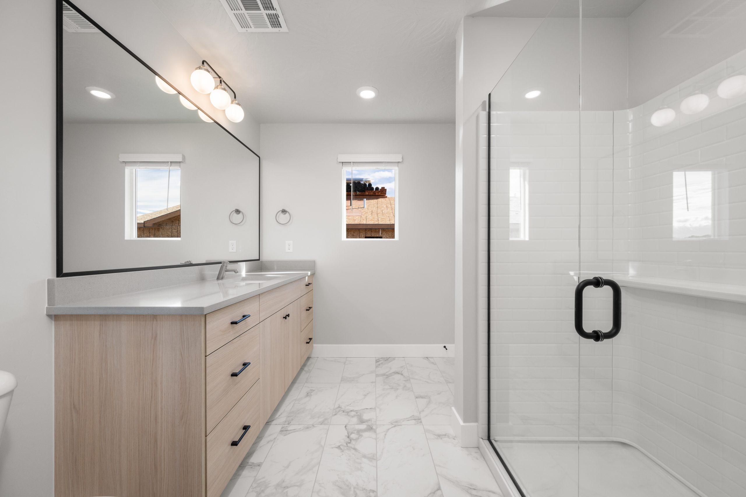 Modern primary bathroom with an oversized vanity, marble-look tile flooring, and glass shower enclosure at Rise in Washington, Utah.