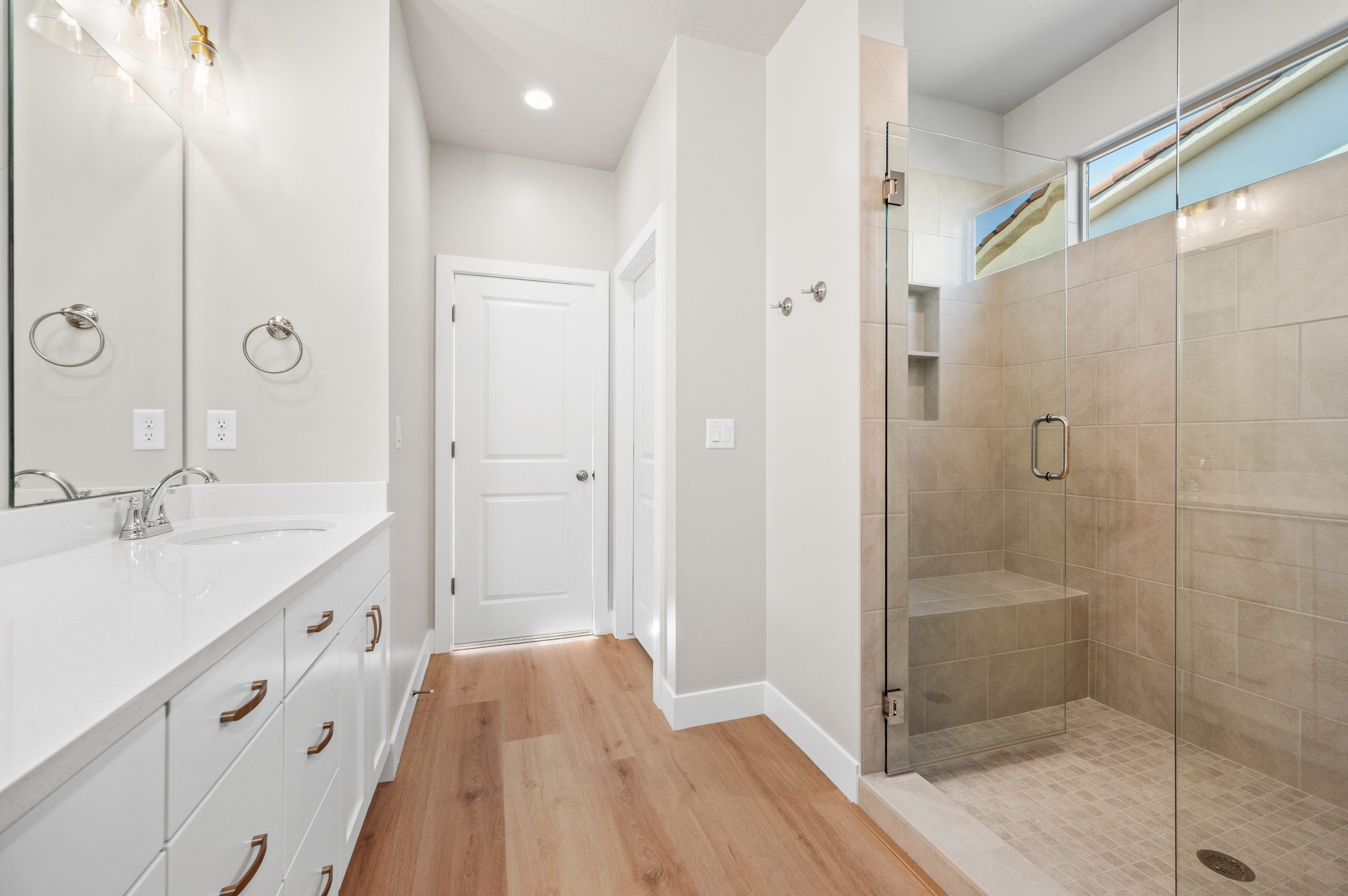Modern primary bathroom with a glass-enclosed walk-in shower, built-in shower bench, and white vanity in the Mojave home at Solis in Washington, Utah.