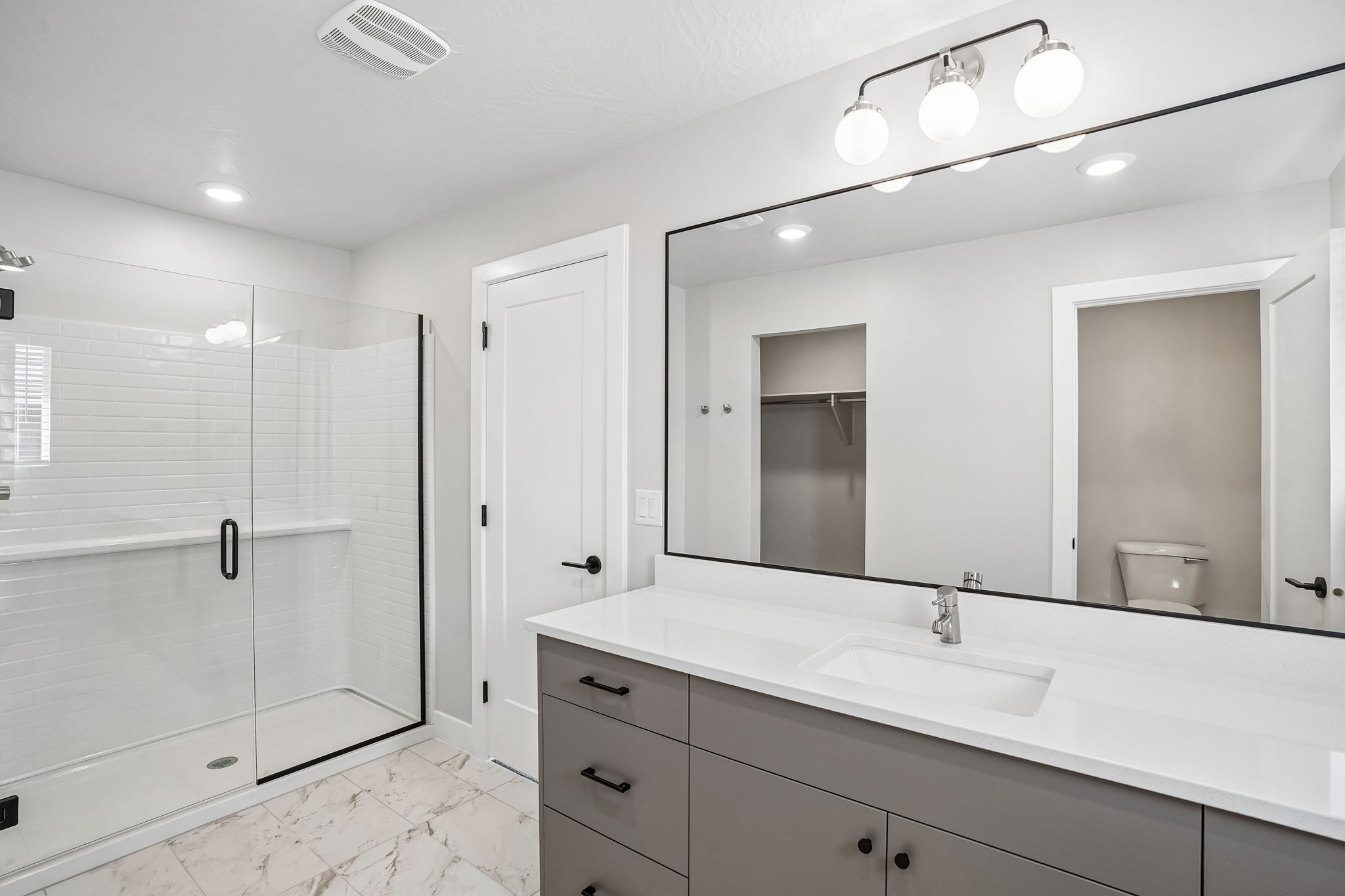 Modern primary bathroom in the Sunburst floor plan at Rise in Washington, Utah, featuring a glass-enclosed shower, white subway tile, and contemporary vanity.