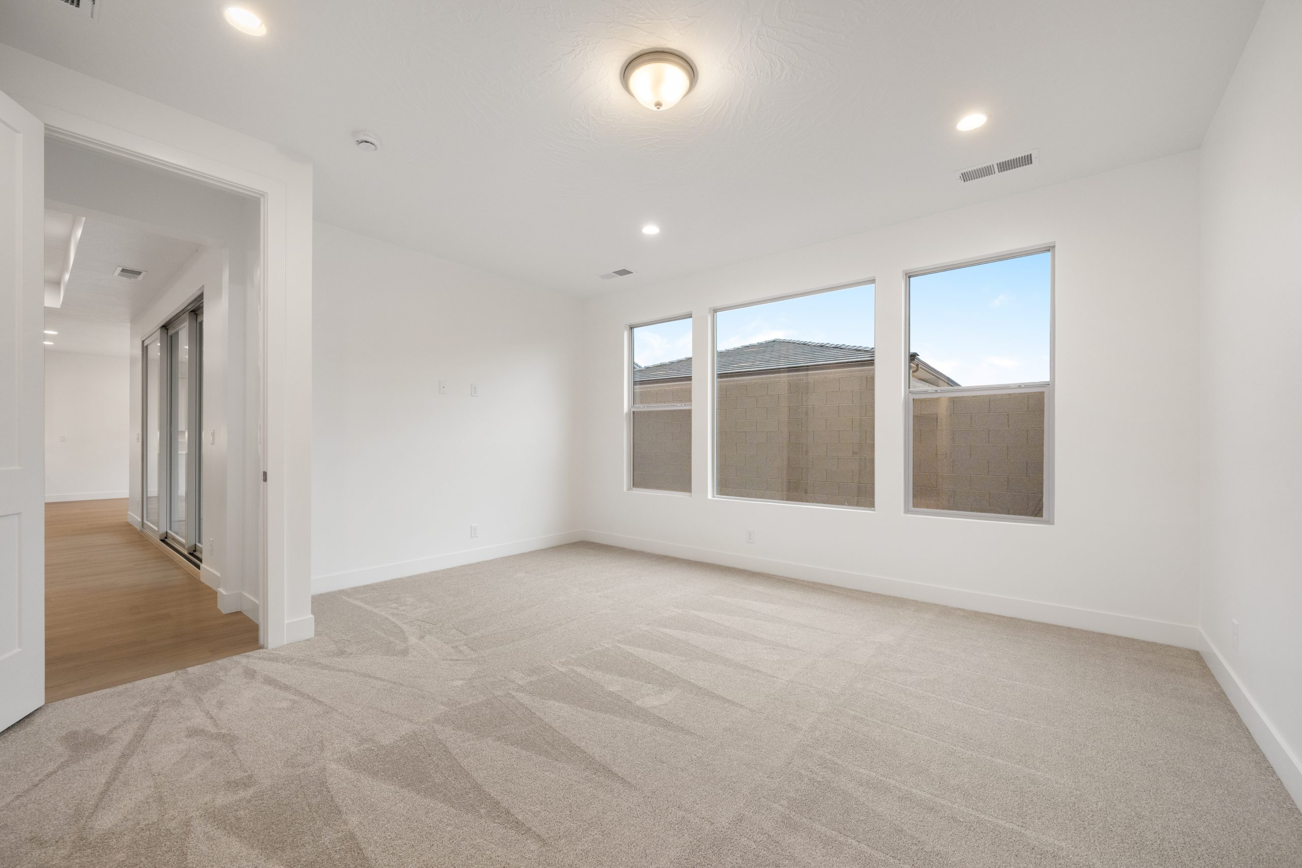 Spacious primary bedroom in the Mesa floor plan at Solis in Washington, Utah, featuring neutral carpeting, three large windows, and natural light.