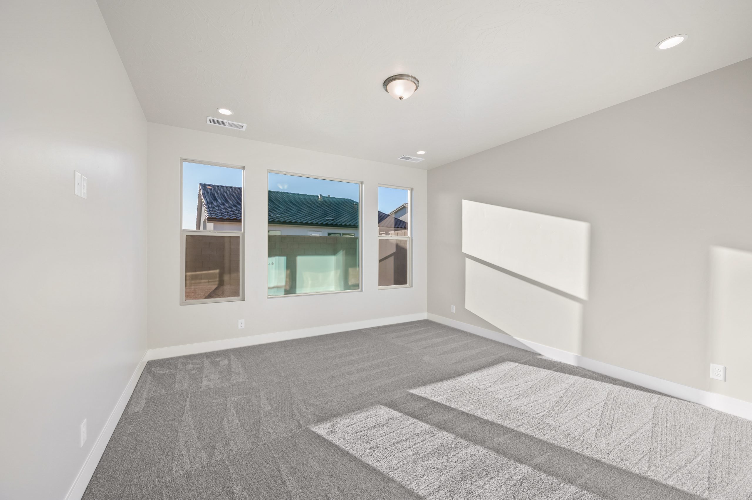Spacious primary bedroom featuring three large windows, soft neutral carpeting, and abundant natural light in the Mojave floor plan at Solis.