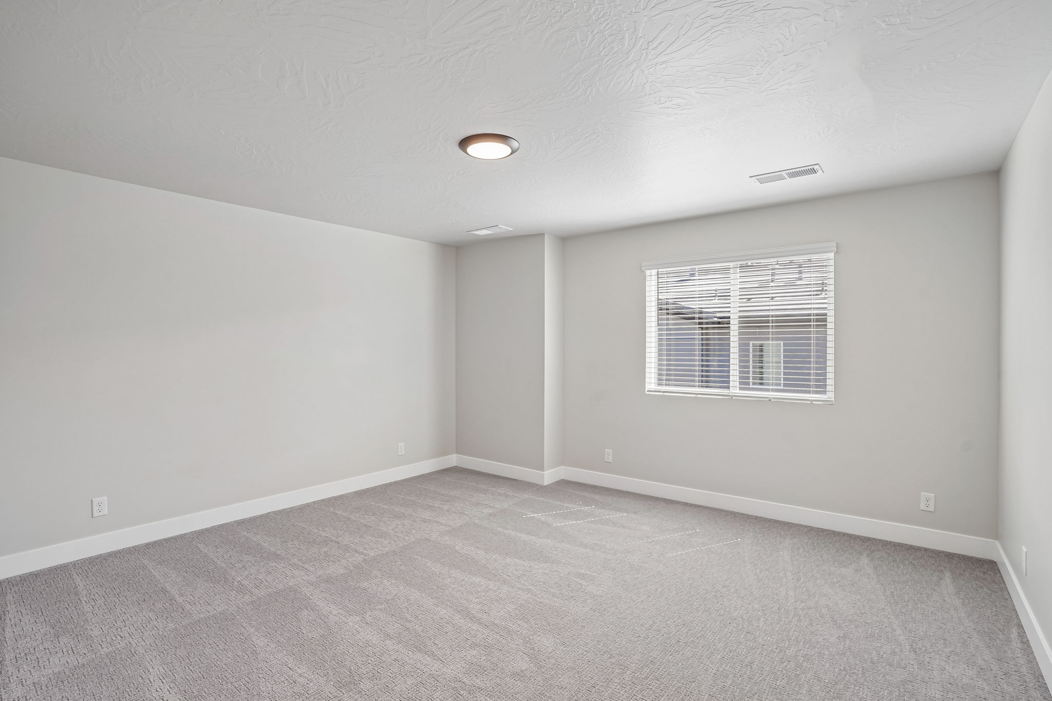 Spacious primary bedroom in the Sunburst townhome by Cole West, featuring soft gray carpeting, neutral walls, and a large window providing natural light.