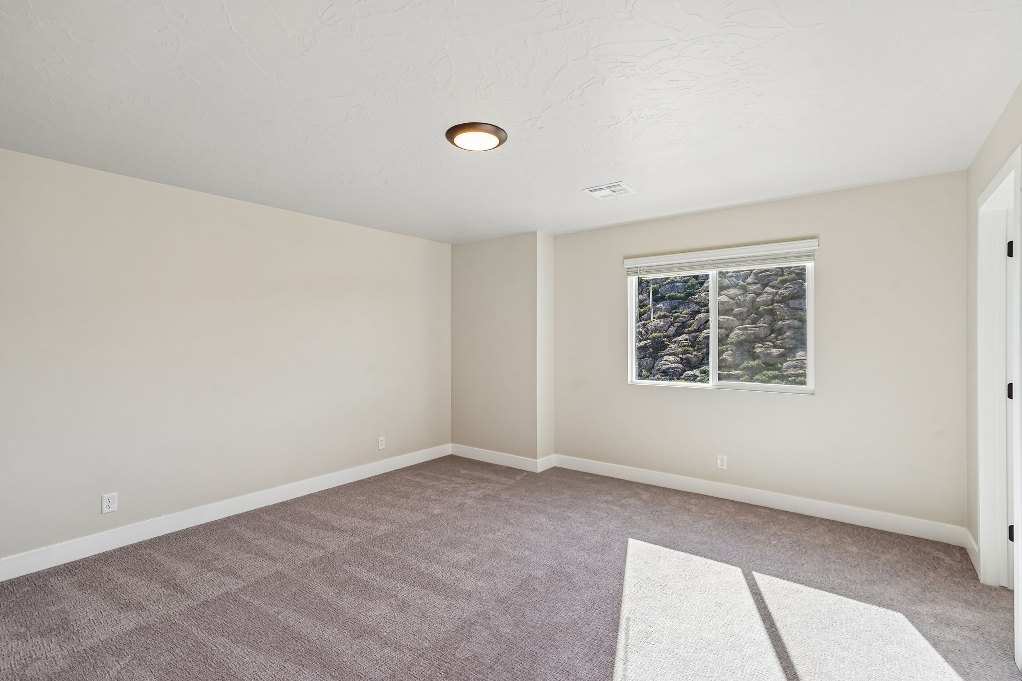 Bright primary bedroom featuring plush carpeting, neutral finishes, and natural rock views.