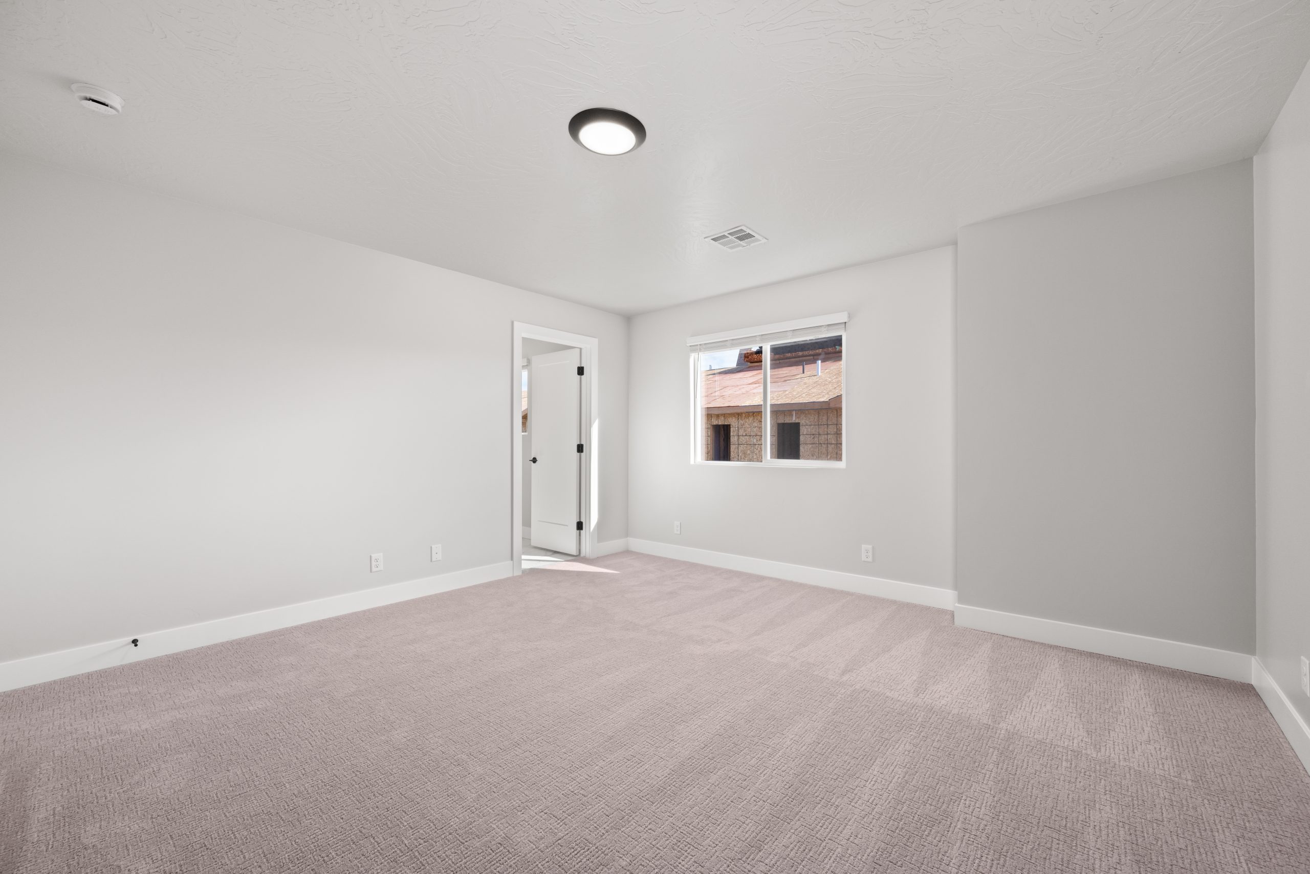Bright primary suite featuring a large window, neutral carpeting, and a spacious layout in the Sunrise floor plan in Washington, Utah.
