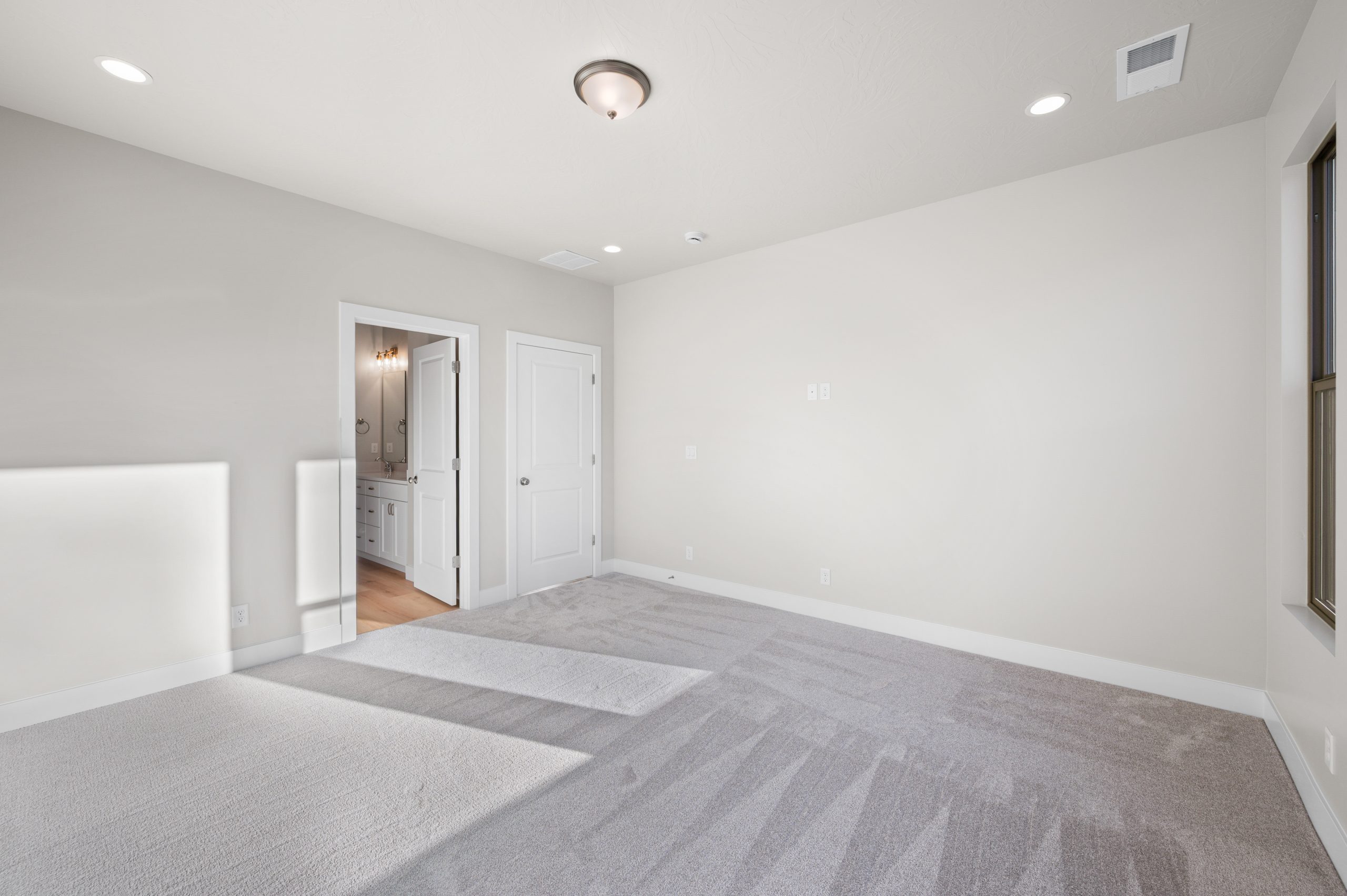 Bright primary suite with plush carpeting, neutral finishes, and direct access to the primary bathroom in the Mojave home by Cole West.